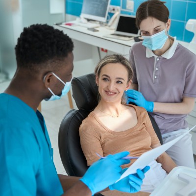 Zahnzusatzversicherung ohne Gesundheitsfragen: Ein Zahnarzt erklärt einer Patientin im Behandlungsstuhl etwas.