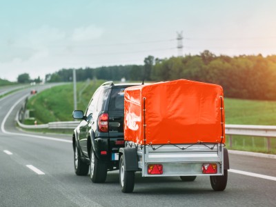 Anhänger-Versicherung: SUV mit kleinem Anhänger mit orangener Plane auf der Autobahn 